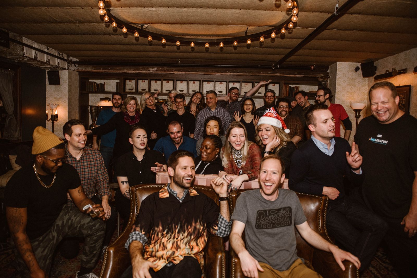 Griff with a large group of smiling people in a lounge with string lights